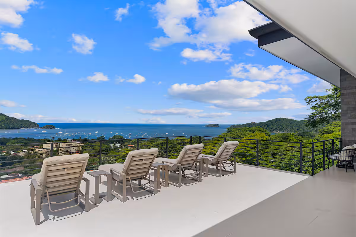 Terrace with lounge chairs overlooking ocean, mountains in background.