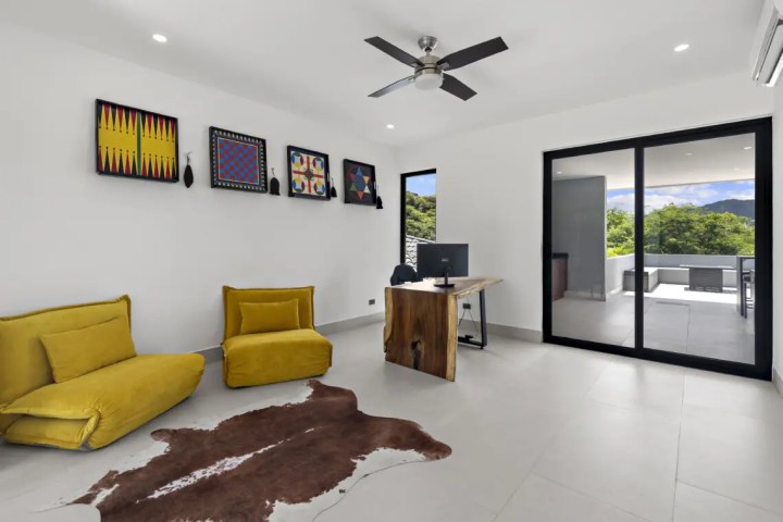 Modern room with yellow chairs, wooden desk, wall art, ceiling fan, and balcony view.