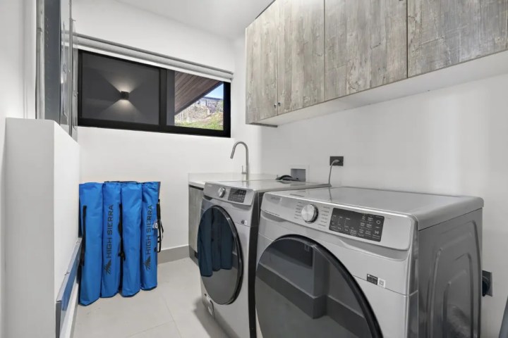 Laundry room with washer, dryer, sink, and blue bags by a window.