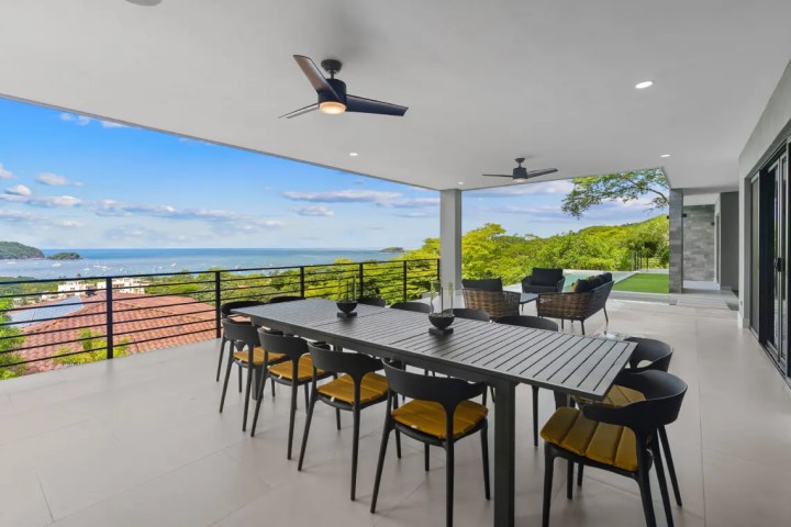 Outdoor patio with dining table, chairs, ceiling fans, and ocean view.
