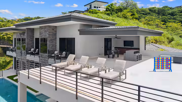 Modern hillside house with patio, lounge chairs, pool, and a giant Connect Four game.