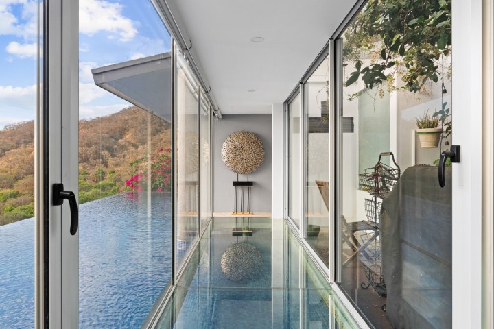 Glass-walled hallway with a view of trees and a round wall sculpture.