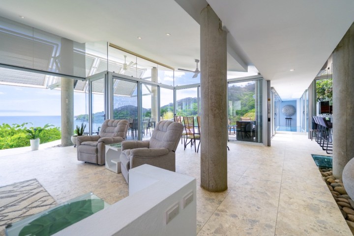 Modern living room with ocean view, large windows, and beige furniture.