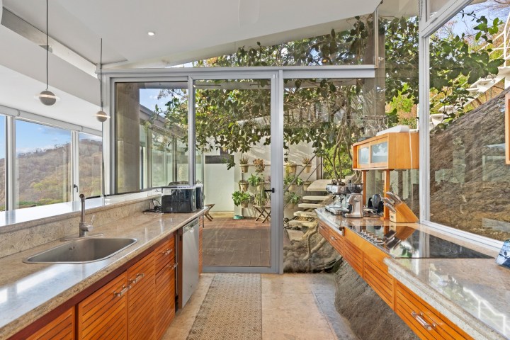 Modern kitchen with wooden cabinets, stone countertops, and a glass door leading to an outdoor area.
