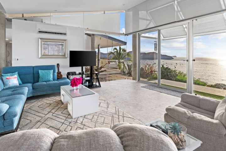 Modern living room with ocean view, blue sofas, TV, and large windows.