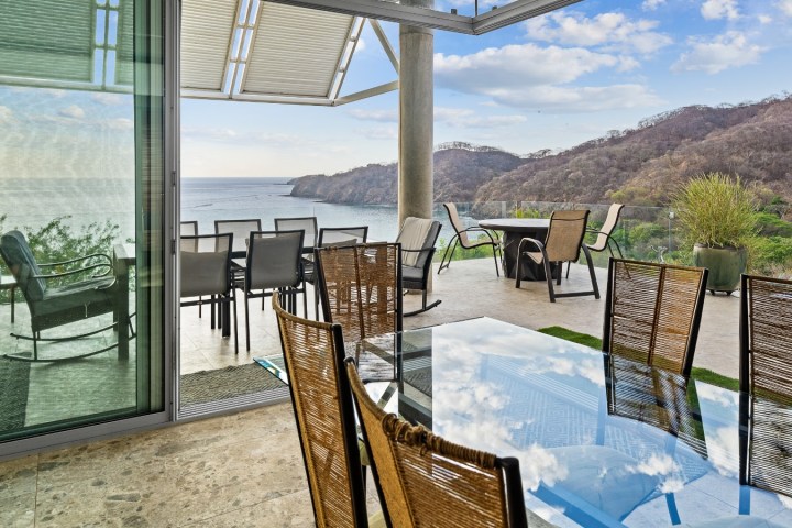 Outdoor patio with glass table, wicker chairs, ocean and mountains view.