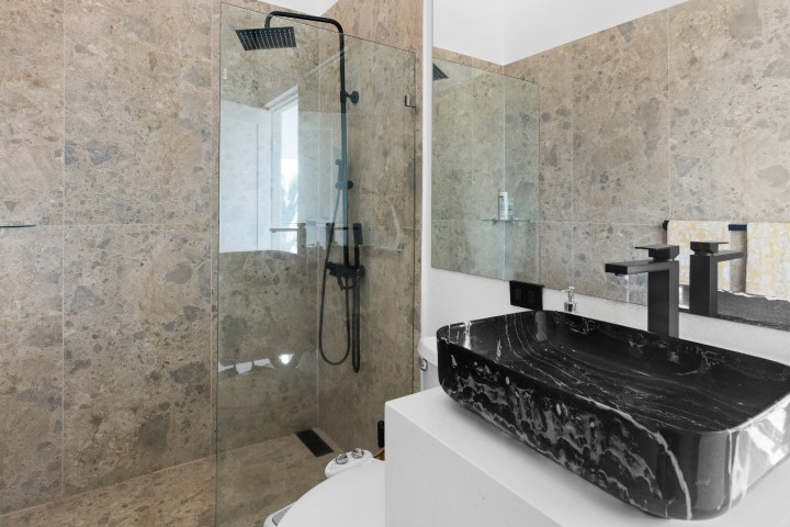 Modern bathroom with black sink, glass shower, and marble walls.