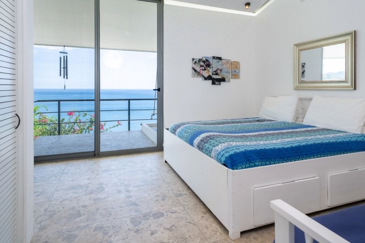 Bright bedroom with blue bedspread, sea view and sliding glass door.
