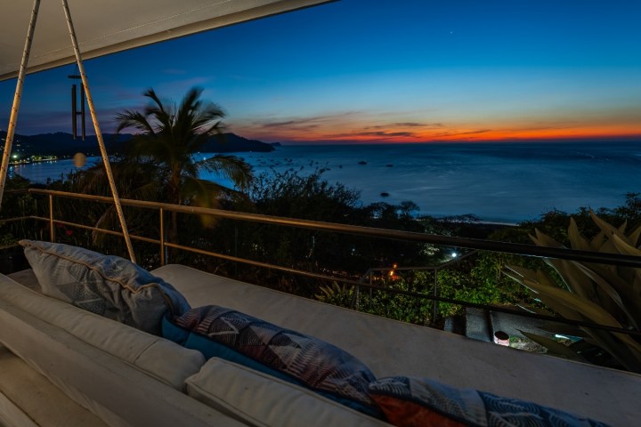 Outdoor patio with couch overlooking a sunset over the ocean.