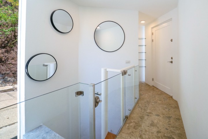 White hallway with circular mirrors on the wall and glass railing.