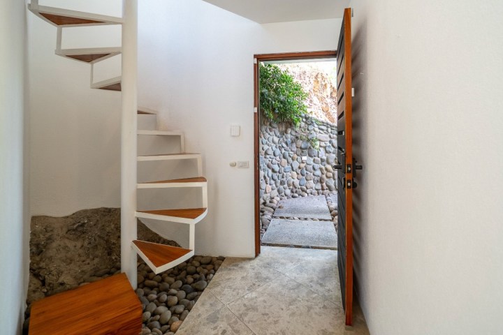 Open door with stone path, spiral stairs, and white walls.