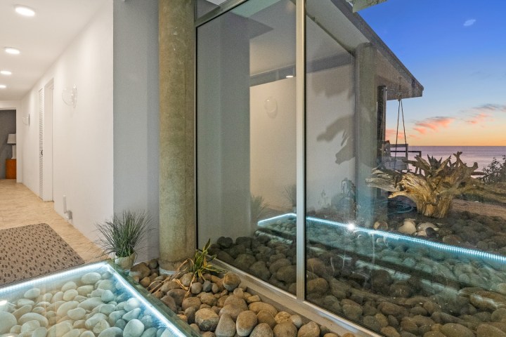 Modern hallway with glass walls, pebble floor, and ocean sunset view.