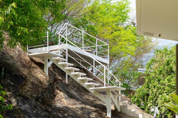 White staircase on a rocky slope surrounded by green trees.