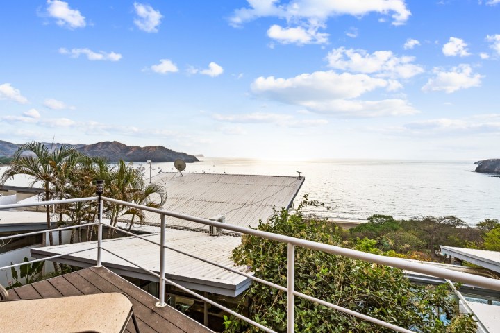 Ocean view from balcony with railing, scenic coastline, and blue sky.