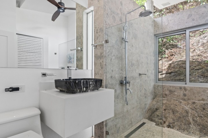Modern bathroom with stone walls, black sink, and glass shower.