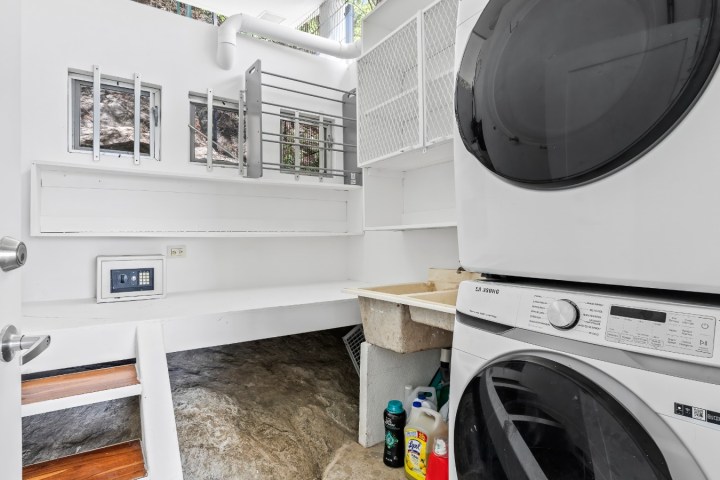 Small laundry room with stacked washer and dryer, sink, and cleaning supplies on floor.