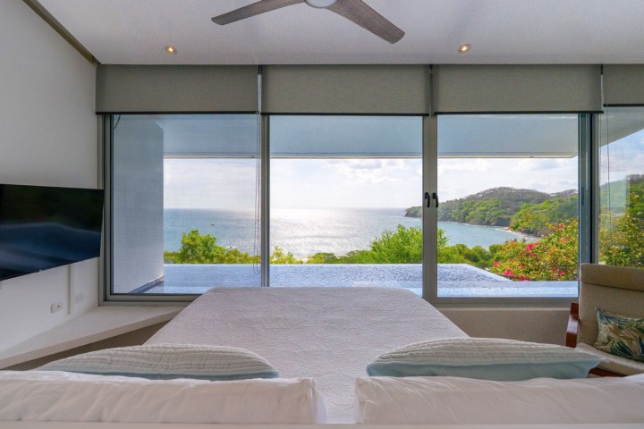 Bedroom with ocean view, large windows, TV, and ceiling fan.