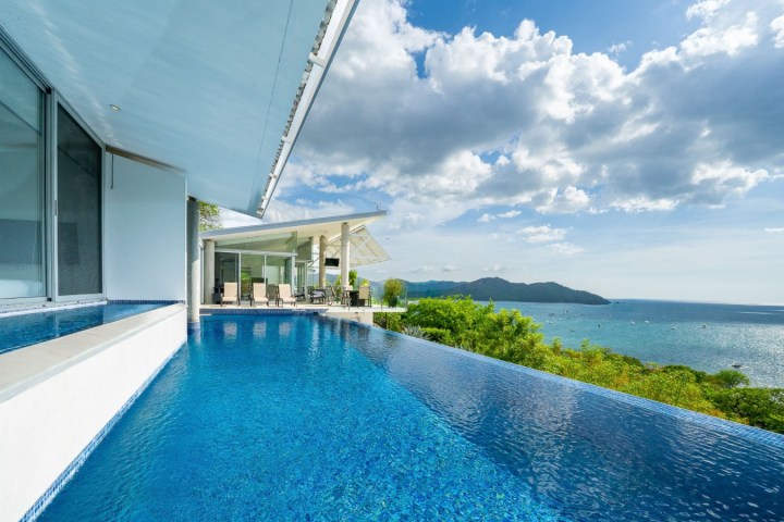 Infinity pool overlooking ocean with blue sky and clouds.