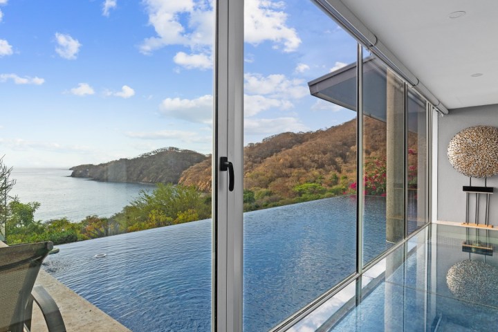 Infinity pool with ocean view through glass wall in a modern room.