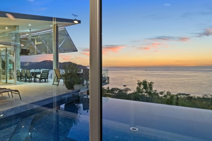 Modern house with a pool overlooking ocean at sunset.