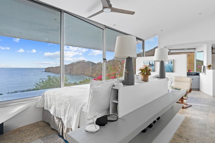Modern bedroom with ocean view, large windows, and minimalist decor.