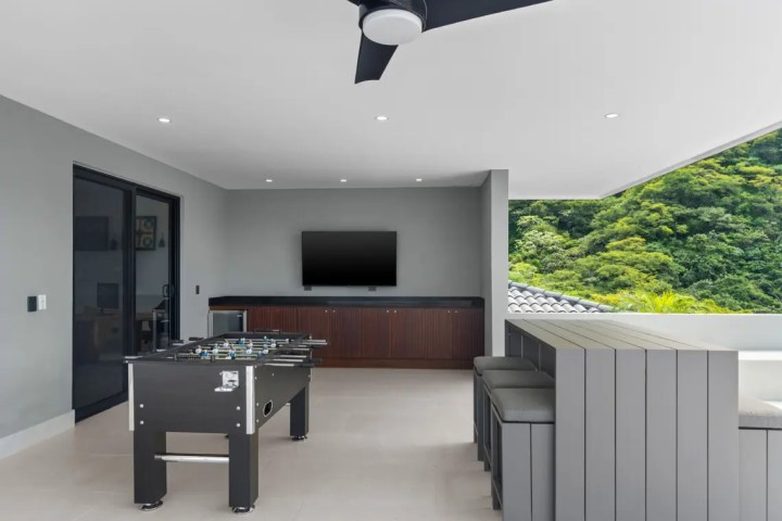 Modern room with TV, foosball table, and seating area overlooking greenery.