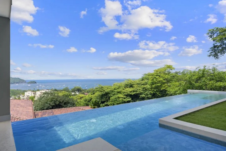 Infinity pool overlooking ocean with lush greenery and blue sky.