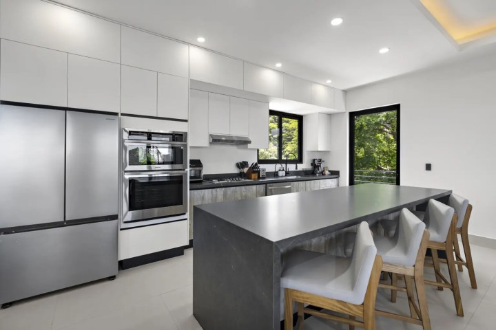 Modern kitchen with white cabinets, stainless steel appliances, and a gray island with four chairs.