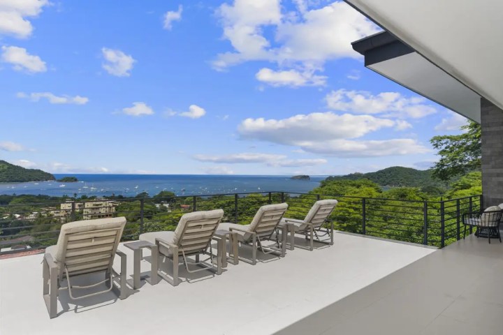 Rooftop deck with lounge chairs overlooking ocean and hills.