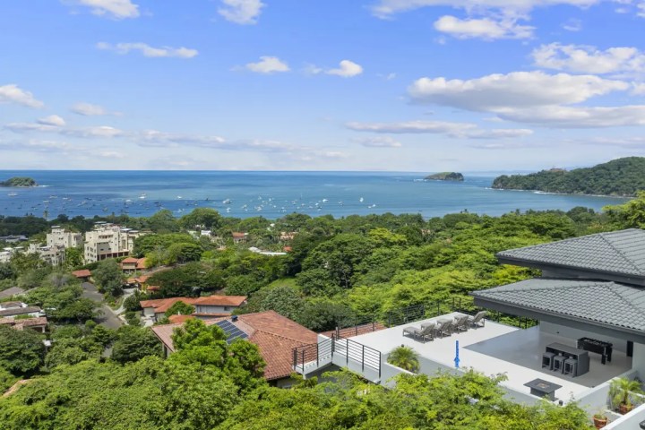 Scenic view of buildings, trees, and ocean under a cloudy sky.