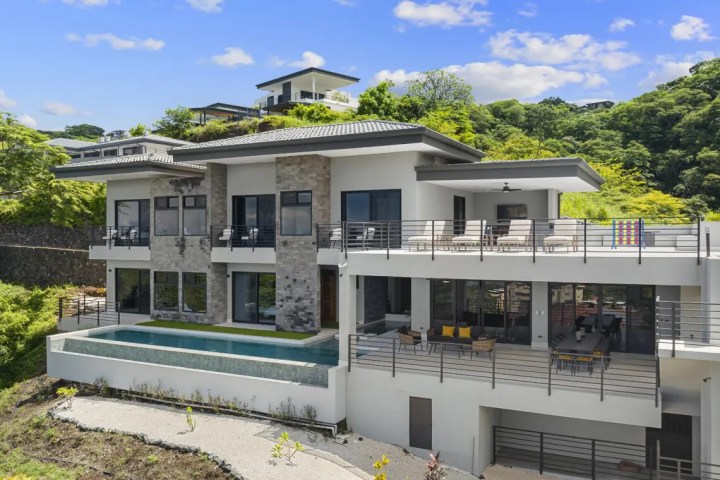 Modern hillside house with large windows, terraces, and a pool.