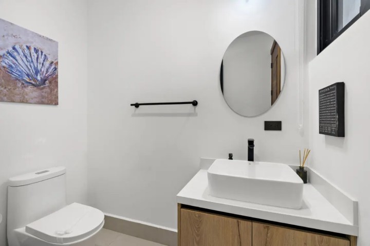 Modern bathroom with round mirror, sink, toilet, and wall art.