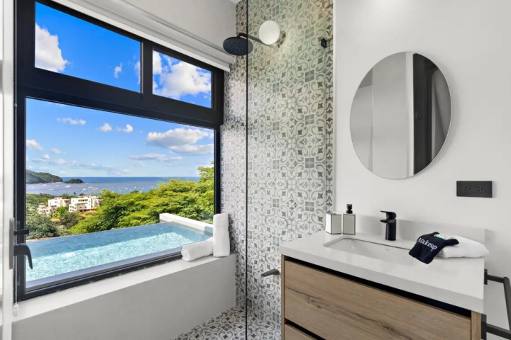 Modern bathroom with ocean view, round mirror, and geometric tiles.