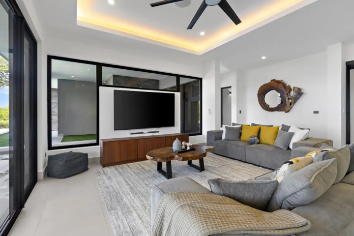 Modern living room with sectional sofa, wall-mounted TV, and large windows.