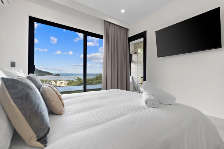 Modern bedroom with ocean view, large window, TV, and bed.