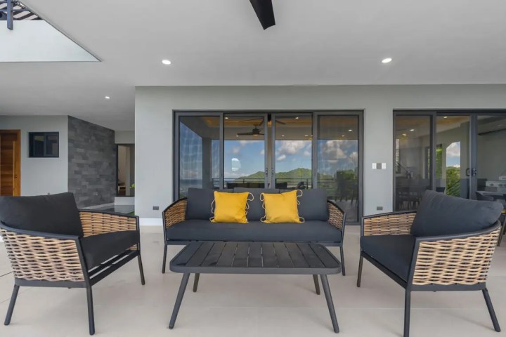 Outdoor patio with wicker chairs, black cushions, and yellow pillows.