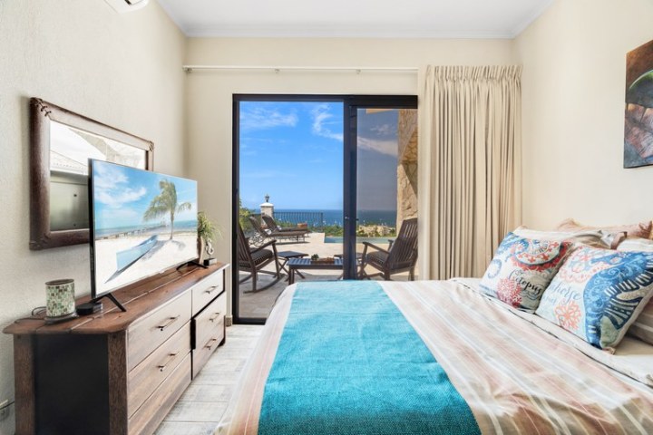 Bright bedroom with ocean view, TV, and balcony access.