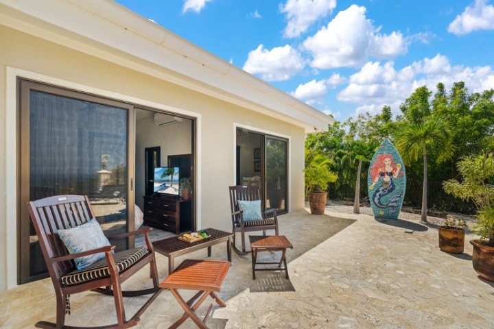 Patio with chairs, small tables, and a mermaid surfboard decoration under a blue sky.