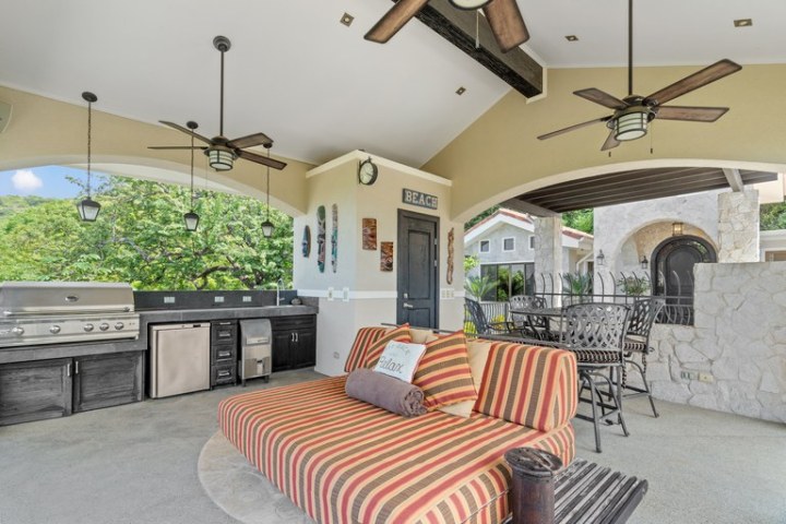 Covered patio with striped seating, grill, fans, and decor.