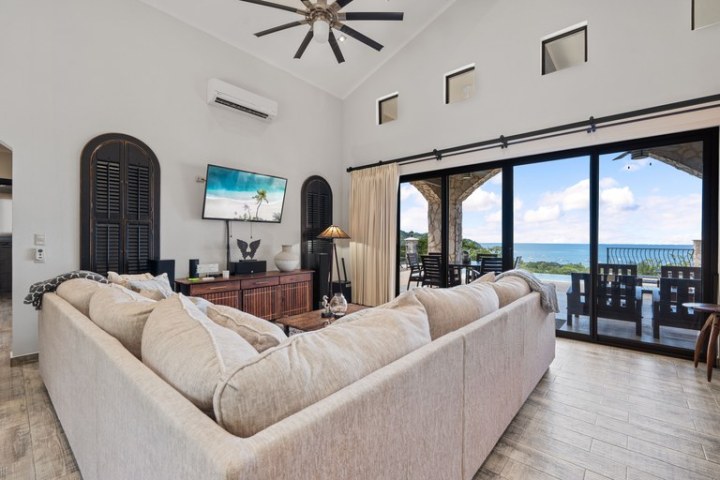 Living room with beige sectional sofa, wall-mounted TV, large windows, and ocean view.