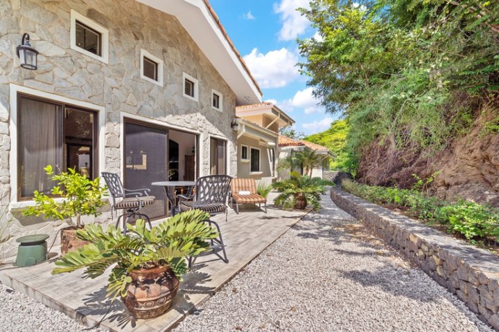 Stone house with patio furniture and plants on gravel path.