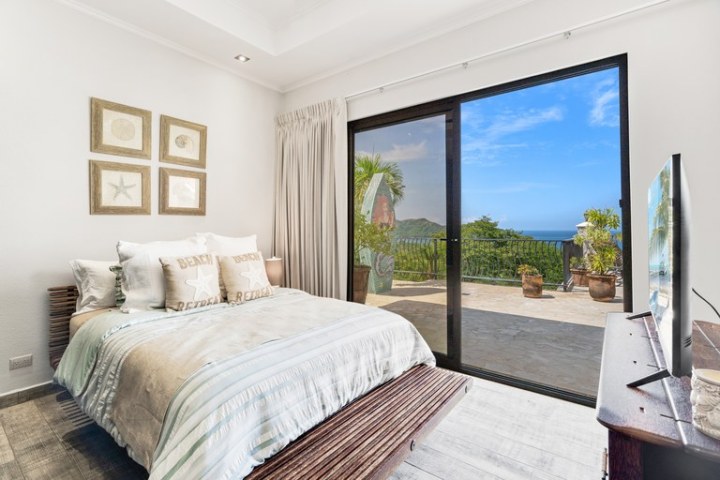 Bedroom with a large bed, decor, and a glass door leading to a patio with ocean view.