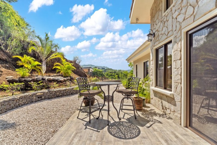 Outdoor patio with metal furniture and stone house wall under a blue sky.
