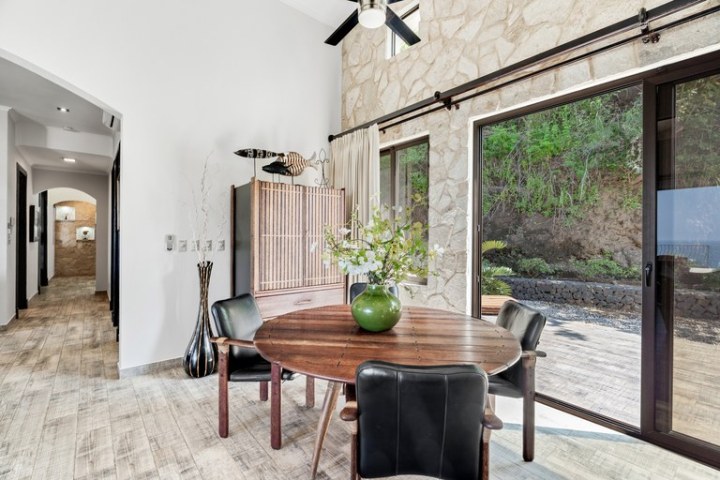 Modern dining area with round table, four chairs, stone wall, and large glass doors to patio.