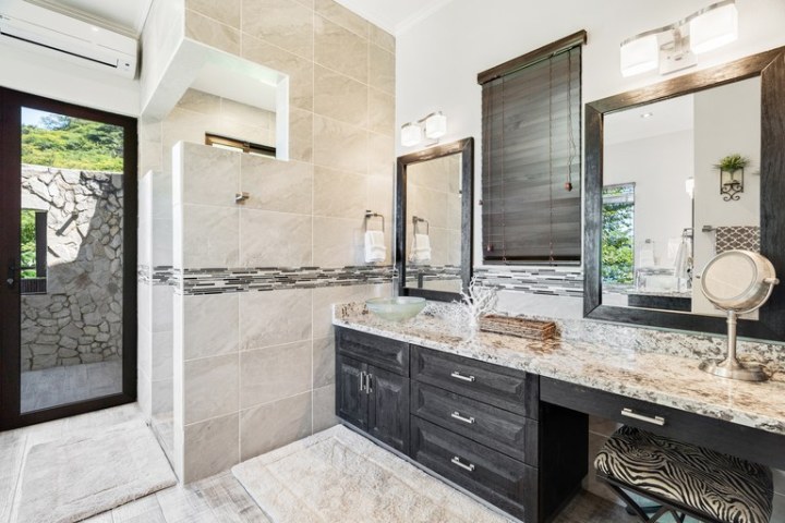 Modern bathroom with dual sinks, large mirror, and glass shower featuring tile walls and stone accents.