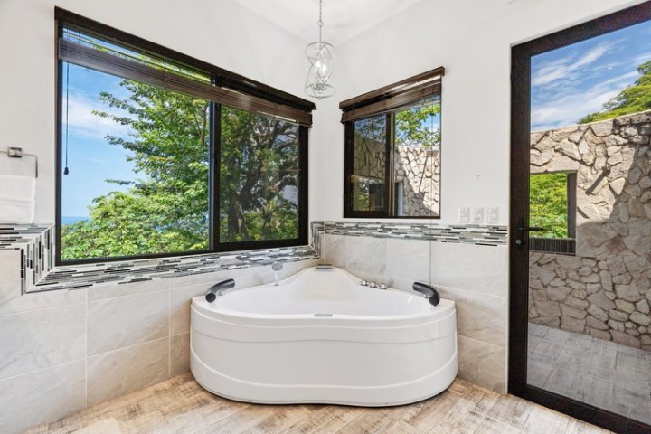 Corner bath with large windows, views of trees, stone wall outside.