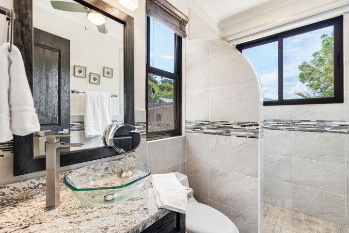 Modern bathroom with glass sink, tiled shower, and large window overlooking trees.