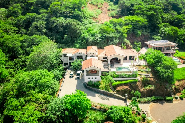 Aerial view of a large house with a pool surrounded by lush greenery.