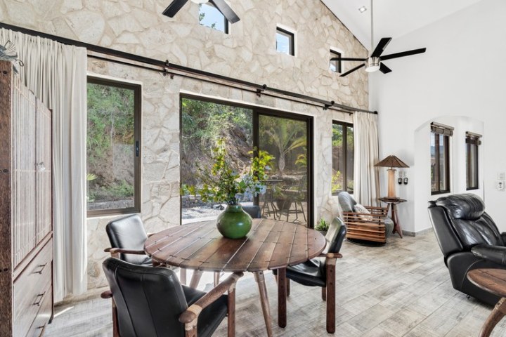 Bright room with stone walls, large windows, wooden round table, chairs, and leather recliners.