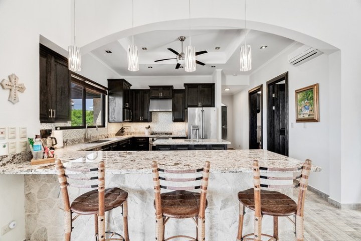 Modern kitchen with granite island, wooden chairs, and dark cabinets.
